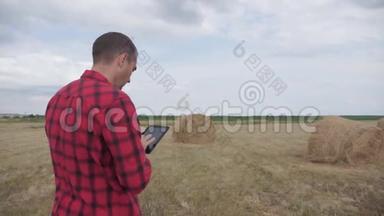 智慧<strong>农业</strong>理念.. 一位农民在一片田野上研究干草堆，研究生活方式，一台<strong>数字</strong>平板电脑。 慢动作